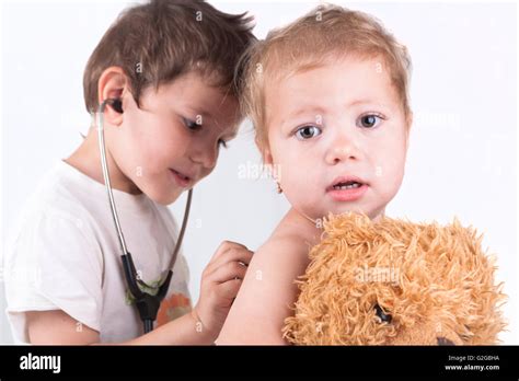 Two Children Playing Doctor With A Red Stethoscope And A Teddy Bear