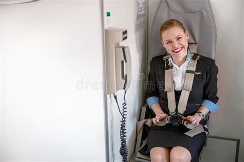 Cheerful Female Flight Attendant Sitting In Chair In Airplane Stock