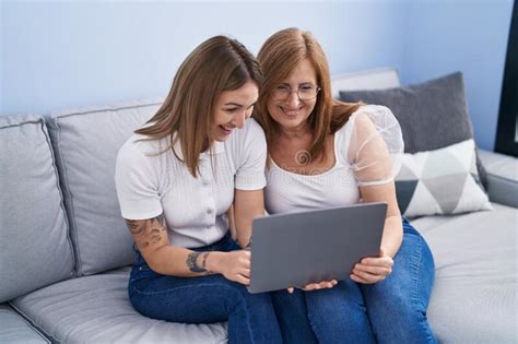 Mother And Daughter Using Laptop Sitting On Sofa At Home Stock Image