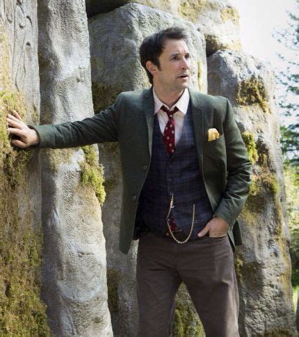 a man in a suit and tie standing next to large rocks with his hands out