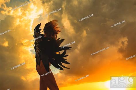 Naked Woman Wrapping Up In Black Paper Wings On Magic Cloudy Sunset Sky