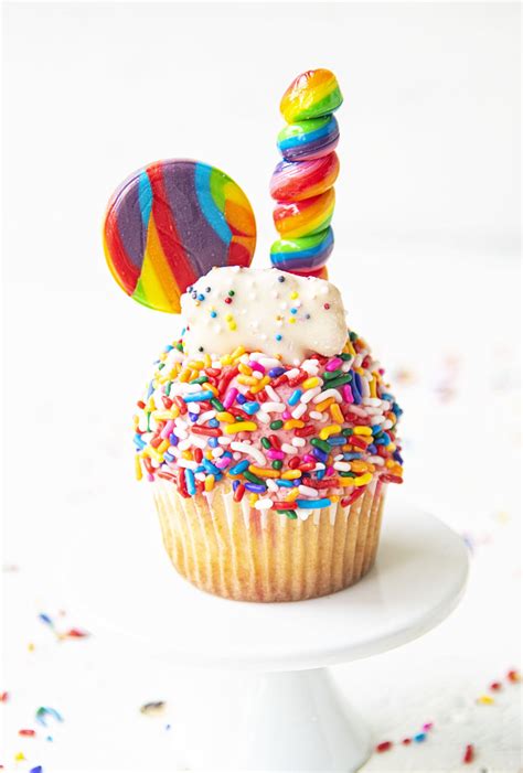 A Cupcake Topped With Sprinkles And A Rainbow Candy Lollipop