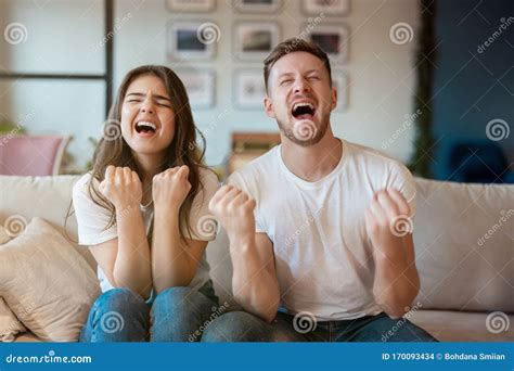 Young Couple Man And Woman Sitting On The Sofa Both Looking Winning