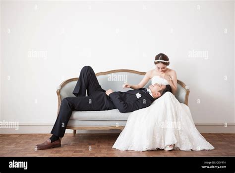 Smiling Bride Sitting On Sofa And Groom Lying Down On Her Lap Stock