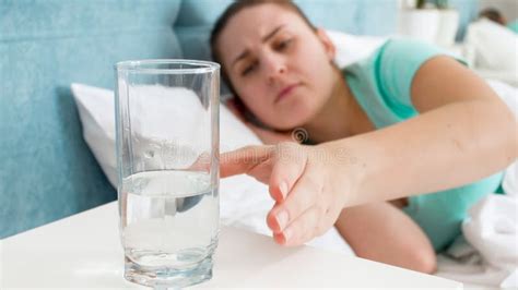 Portrait Of Sick Woman Taking Glass Of Water From Bedside Table Stock