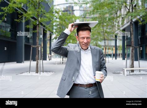 Smiling Mature Businessman Holding Laptop On Head Standing Outside