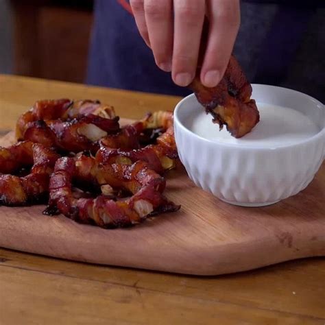 Someone Is Dipping Bacon Into A Bowl On A Wooden Cutting Board With