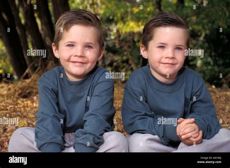 Young Identical Twin Boys In Matching Outfits While Outdoors Sitting