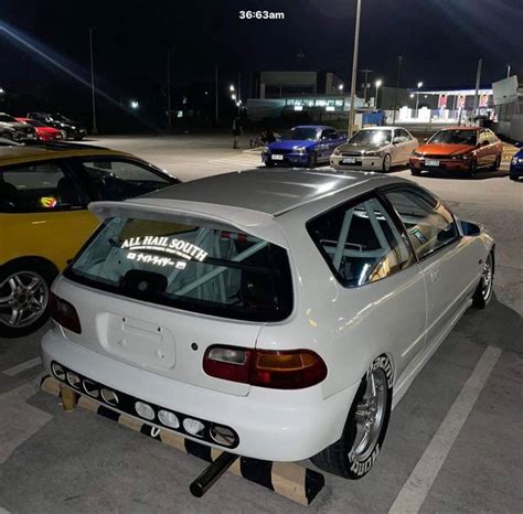 several cars are parked in a parking lot at night, one is white and the other is yellow