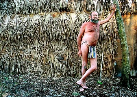 A Naked Man Standing Next To A Tree In Front Of A Thatched Hut With No