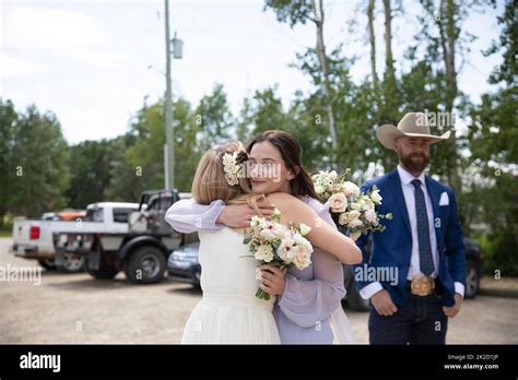 Bride And Maid Of Honor Hugging In Parking Lot On Wedding Day Stock