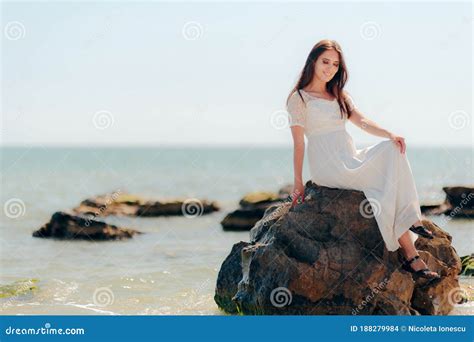 Woman With Long Dress Sitting On Rocks By The Sea Stock Photo Image