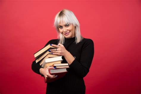 Modelo De Jovem Segurando Muitos Livros Em Uma Parede Vermelha Foto