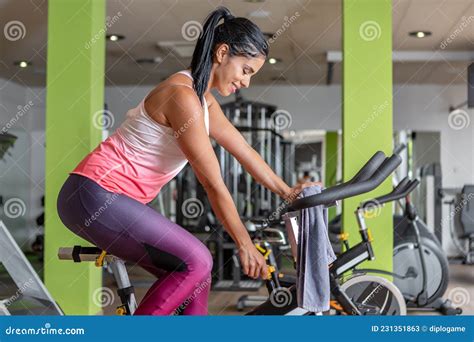 Vista Lateral De Una Joven Deportista Latina Ajustando Una Bicicleta Estacionaria Mientras Hace