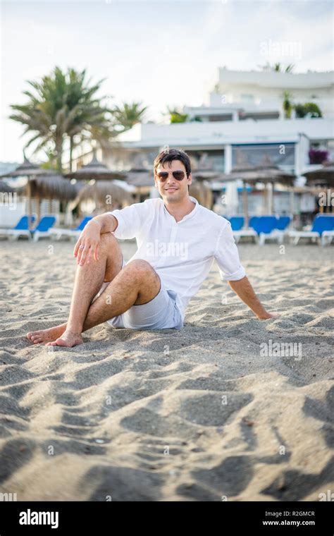 Portrait Of Handsome Man Sitting Relaxed On The Beach By Sunset Stock