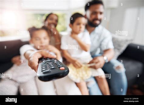 Closeup of remote control with family watching tv in their living room ...