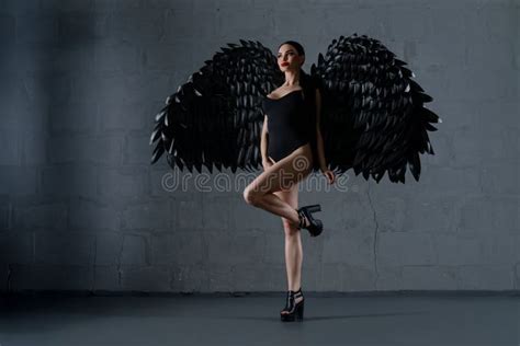 Woman Wearing Lingerie With Black Wings Poses Confidently In A Studio Setting Stock Photo