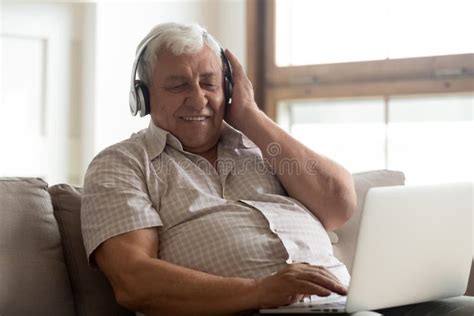 Smiling Older Man Wearing Wireless Headphones Enjoying Music Using