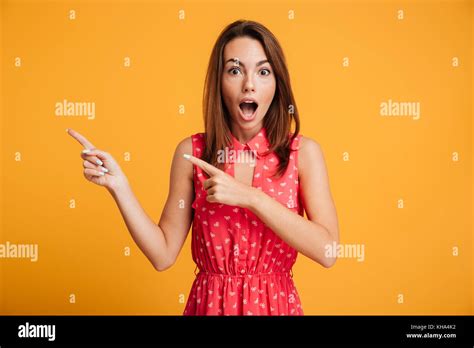 Shocked Brunette Woman In Dress Winks And Pointing Up While Looking At