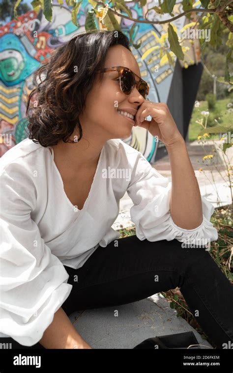 Young Brunette Latina Woman With Short Hair And Curls Smiling Sitting And Wearing Sunglasses