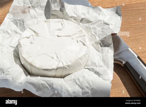 Open Paper Package Of Whole Head Of Camembert And A Knife Under A