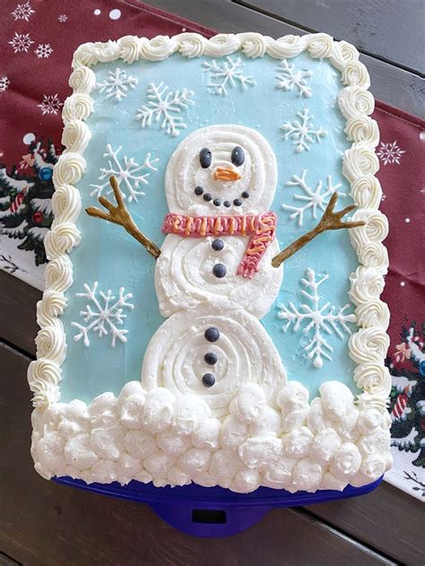 A Frosted Snowman Is In The Middle Of A Blue And White Cake With Icing