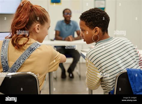 Back View Portrait Of Two Teenage Girls Whispering In School Classroom