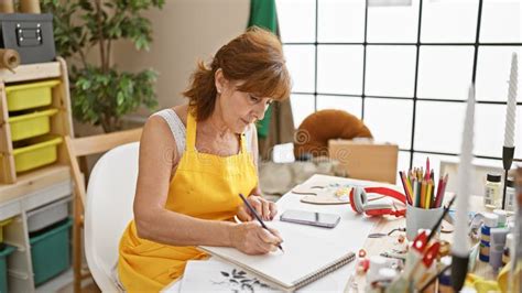 Mature Woman Artist Sketching In A Bright Studio Wearing An Apron With