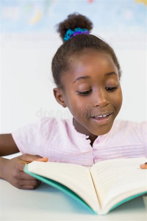 Menina Da Escola Que Guarda Um Livro Na Sala De Aula Imagem De Stock