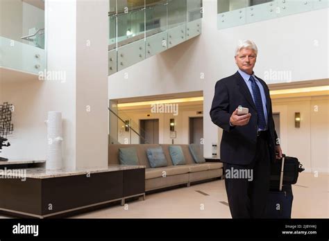 Mature Caucasian Man Holding Cell Phone Walking Through Hotel Lobby