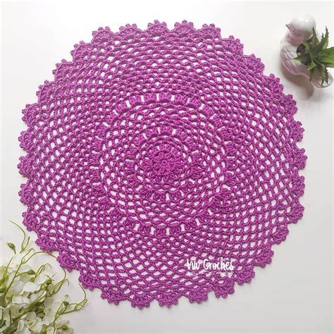 A Crocheted Doily Sits On A Table Next To Flowers