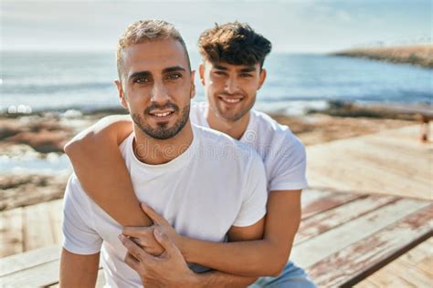 Jovem Casal Gay Sorrindo Feliz Sentado No Banco No Palco Da Praia Foto