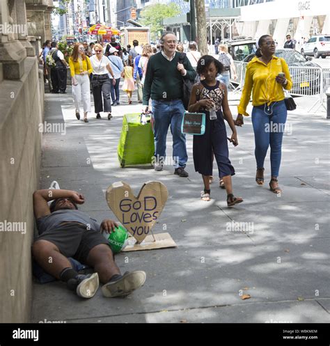 Homeless Man With A Sign God Loves You Rests On The Sidewalk While