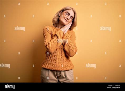 Middle Age Beautiful Blonde Woman Wearing Casual Sweater And Glasses Over Yellow Background