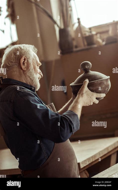 Senior Potter In Apron Examining Ceramic Bowl At Workshop Stock Photo
