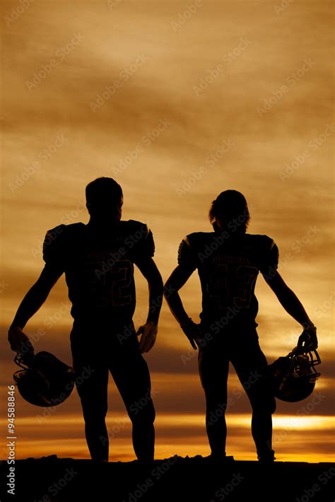 Silhouette Of Football Players Holding Helmets In The Sunset Stock