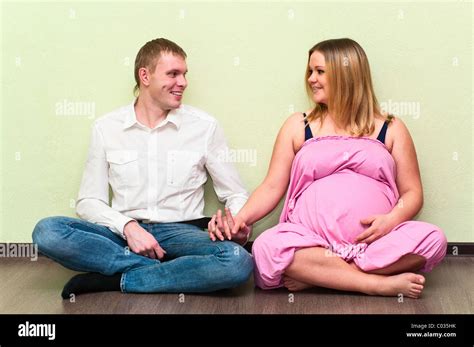 Pregnant Woman With Her Husband Sitting On Floor In Empty Room