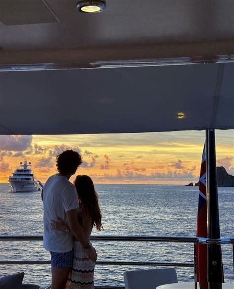 A Man And Woman Standing On The Deck Of A Boat At Sunset