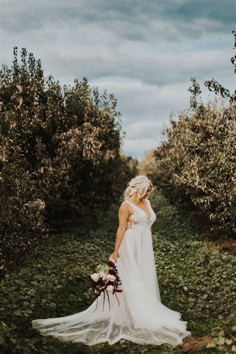 A Woman Standing In An Apple Orchard Wearing A Wedding Dress