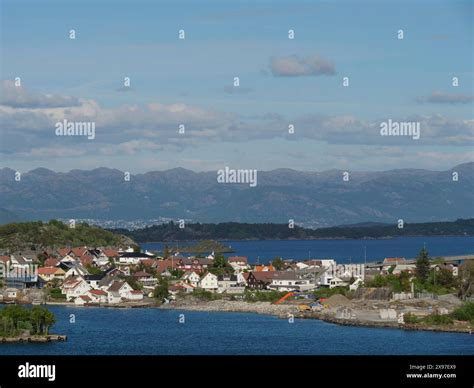 City along a fjord, surrounded by mountains and clouds, with clear blue sky, houses on small ...