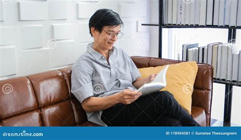 Senior Asian Man Reading Book On Sofa In Living Room At Home Portrait Of Asian Elderly Man Is