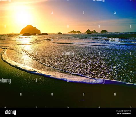 Bright Setting Sun Sinking Below The Horizon Over The Water With Rock