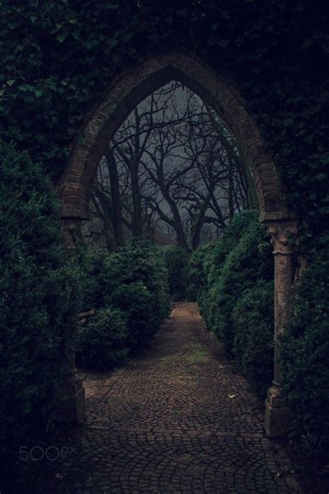 An Arch In The Middle Of A Brick Walkway With Trees And Bushes On