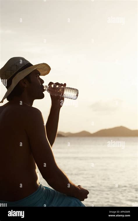 Young man drinking water on beach Stock Photo - Alamy