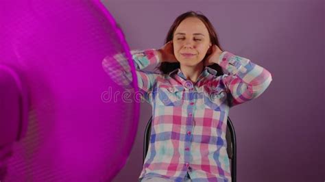 Acercamiento De Una Joven Sentada En Una Silla Frente A Un Ventilador Con Fondo Morado Brunette