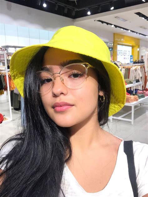 A Woman Wearing A Yellow Hat And Glasses In A Clothing Store Looking