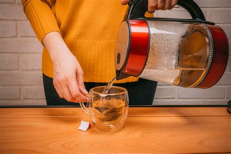 Premium Photo Woman Pouring Hot Water From A Kettle Into A Clear Glass Mug