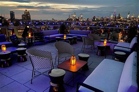 An Outdoor Seating Area Overlooking The City Skyline At Night With Lit