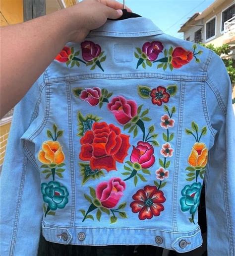 Someone Is Holding Up A Jean Jacket With Flowers On It And The Back Has