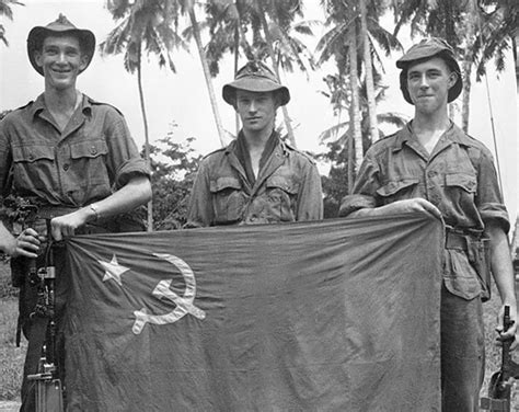 3 British Soldiers Hold Up A Flag Taken From Malayan Communist